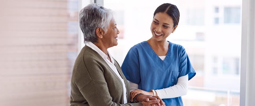 Smiling female nurse walking arm in arm with an elderly female resident