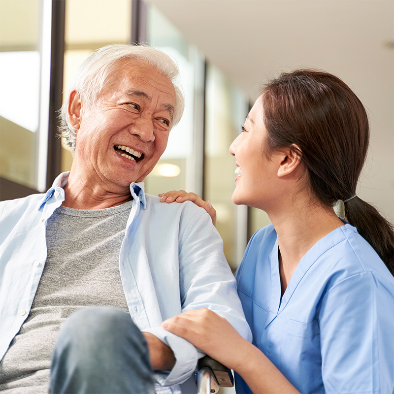 Nurse leaning down to speak with a resident seated on a chair